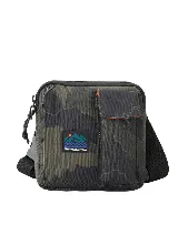 Bolso de mano y bandolera Rip Curl modelo 24/7 Pouch Search Camo, con diseño de camuflaje en tonos verde militar y negro. Cuenta con un compartimento principal con cierre, un bolsillo frontal con solapa, correa ajustable y el parche con el logo de la marca en la parte frontal.