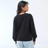 Sweater de punto negro con diseño cruzado tipo cárdigan, escote en V profundo y cierre lateral con un botón decorativo grande de efecto carey. Presenta mangas largas con puños ajustados.