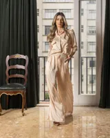 Conjunto de camisa y pantalón color nude de satén. La camisa es de manga larga con cuello clásico, cierre frontal con botones y bolsillos con solapa en el pecho. El pantalón es de corte palazzo con cintura elástica ajustable con cordón.