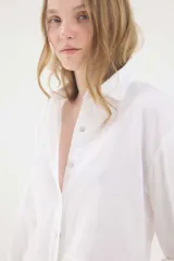 Camisa de lino blanca, de silueta oversize y calce relajado, con mangas largas y detalles de puntillas en la delantera.