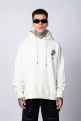 Buzo tipo canguro de corte oversize, color blanco, con capucha y cordones ajustables. Presenta un pequeño estampado de una rosa roja en el pecho y un bolsillo frontal tipo canguro.