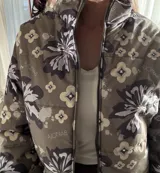 Campera puffer color verde militar con estampado floral grande y detalles geométricos, cuello alto y cierre frontal con cremallera.