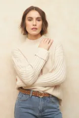 Polera de tejido de punto color beige, con cuello alto, mangas largas con puños acanalados y detalle de trenzas en los hombros.