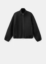 Chaqueta negra de diseño estructurado, con cuello alto, cierre frontal de cremallera metálica y mangas abullonadas con puños ajustados.
