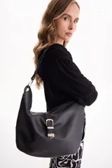 Cartera tipo bolso hobo de cuero sintético negro con textura granulada, asa de hombro ajustable y detalle de tira frontal con hebilla metálica plateada. Cierre superior con cremallera.