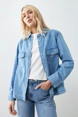Camisa de jean celeste con cuello clásico, cierre frontal con botones a presión, dos bolsillos con solapa abotonada en el pecho y mangas largas con puños abotonados.