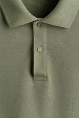 Remera polo H&M de manga corta en piqué de algodón, color verde militar, con cuello camisero y tapeta frontal de dos botones. Corte estándar para una silueta clásica y cómoda.