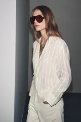 Camisa de algodón color crema o blanco roto, con textura de rayas verticales sutiles. Presenta cuello solapa, escote pico y manga larga.