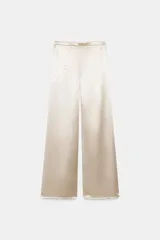 Pantalón de tiro alto y pernera ancha, confeccionado en tejido satinado con aplicación de brillos distribuidos por toda la prenda. Cuenta con cierre lateral mediante cremallera oculta.
