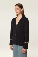 Cárdigan de punto color azul marino, con escote en V, cierre frontal con botones al tono y bolsillos de parche. Presenta mangas largas con aberturas decoradas con cuentas doradas en los puños.