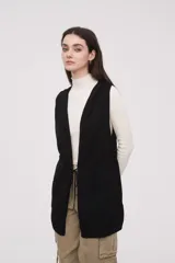 Chaleco largo sin mangas de tejido de punto color negro, con capucha y lazo ajustable en la cintura. Presenta bolsillos frontales y diseño abierto.