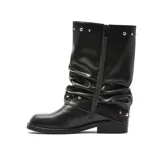Bota de caña media con diseño slouchy, confeccionada en cuero sintético negro. Presenta detalles de tachas metálicas plateadas en la parte superior de la caña y en la base del tobillo, con suela plana y punta redondeada.