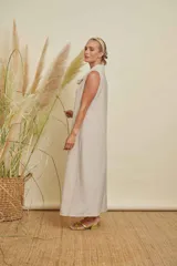 Vestido largo sin mangas, color beige claro con brillo sutil, cuello drapeado y corte recto.