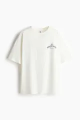 Remera oversized de punto suave de algodón color blanco, con cuello redondo acanalado, hombros caídos y bajo recto. Cuenta con un pequeño estampado tipográfico en azul en el pecho con la frase "La Dolce Vita".