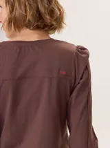 Remera de manga larga color rosado con cuello en V. Presenta detalles de costuras verticales tipo alforzas en el frente y hombros ligeramente fruncidos.