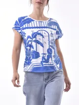Remera de manga corta, cuello redondo, color blanco con estampado en azul que simula una escena tropical vista desde un interior, con plantas y una figura sentada.