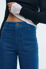 Pantalón de jean de tiro alto, color azul medio, con pierna ancha y corte ajustado en la cadera. Presenta bolsillos de parche tanto en la parte delantera como en la trasera.