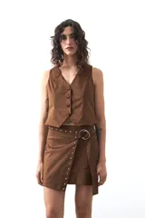 Chaleco de gamuza color marrón, con escote en V y cierre frontal con botones forrados. Tiene un largo a la cintura y silueta definida.