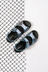 Sandalias chatas con base negra y tiras anchas de cuero sintético color celeste metalizado.