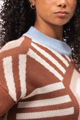 Buzo tejido de punto con diseño geométrico tipo mandala en tonos marrón, beige y blanco. Presenta cuello redondo y puños en color celeste pastel, con corte holgado y mangas largas.