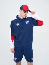 Canguro deportivo Umbro del Club Nacional de Football, modelo Nexo para hombre. Diseño en color azul marino con mangas rojas y detalles en celeste y blanco, capucha con cordón ajustable y bolsillo tipo canguro.