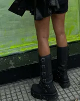 Bota de caña media de cuero negro con plataforma track y múltiples hebillas metálicas.