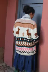 Cardigan tejido a mano en lana merino, con diseño multicolor de inspiración andina que incluye motivos de llamas, franjas geométricas y detalles en tonos beige, marrón, negro y rosa.