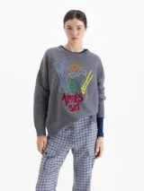 Sweater de lana gris con silueta holgada y cuello redondo. Presenta un bordado frontal colorido con motivos de esquí y la inscripción 'Apres Ski'.