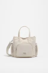 Bolso tipo tote y bandolera de color beige, con bolsillos externos con cierre y asas de mano y hombro.