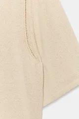 Jersey amplio de punto color beige, con escote redondo y mangas anchas por debajo del codo. Presenta detalles de calados en los laterales.