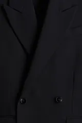 Blazer negro de doble botonadura con solapas de pico, bolsillo superior, bolsillos delanteros ribeteados con solapa, tres bolsillos interiores, botones decorativos en los puños y abertura doble atrás.