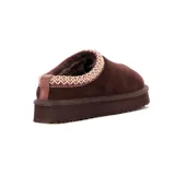 Pantufla tipo mule de cuero gamuzado color marrón, con interior de peluche y detalle de costura decorativa trenzada en el borde superior. Cuenta con una suela de plataforma dentada de goma.