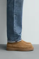 Bota de caña corta fabricada en piel con acabado serraje, con detalle de costura en el empeine, forro interior de pelo sintético y suela plana a tono.