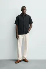Camisa regular fit negra de manga corta, con cuello bowling y cierre frontal de botonadura. Confeccionada en tejido texturizado con elasticidad y aberturas laterales en el bajo.