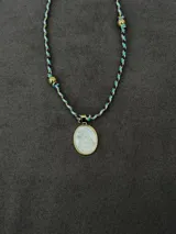 Collar corto con cordón trenzado multicolor en tonos verde, violeta, blanco y dorado, con cuentas esféricas doradas y un dije ovalado de nácar con marco dorado que representa a la Virgen de Luján.