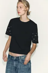 Camiseta de manga corta y cuello redondo, color negro oscuro, con detalle de bordados en forma de espiral con aplicación de abalorios y perlas en las mangas.