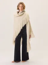 Triángulo de lana color beige con maxi flecos, diseñado por Margara Shaw en colaboración con Manos del Uruguay. Confeccionado con una mezcla de lana merino, mohair, viscosa, algodón y otras fibras, incluyendo lurex y un hilado teñido a mano con lentejuelas.