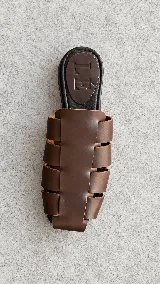 Zuecos de cuero marrón con diseño de tiras anchas entrelazadas estilo romano, punta cuadrada y plantilla plana negra con logo grabado de la marca.