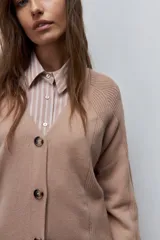Cardigan de punto color beige, con escote en V, cierre frontal con botones oscuros y mangas largas con detalles de tejido en relieve.