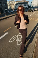 Chaqueta corta de color marrón oscuro, con cuello de solapa, manga larga con trabillas en los puños, bolsillos delanteros con solapa y cierre frontal con botones.