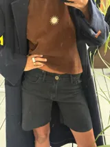 Bermuda de jean negro, tiro medio, con dobladillo deshilachado y botón metálico dorado con logo.