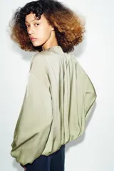 Cazadora bomber fluida de color verde, con cuello redondo, manga larga abullonada, bolsillos frontales y cierre de cremallera metálica.
