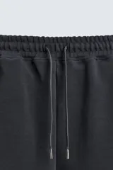 Bermuda estilo jogger de ajuste relajado, color negro, confeccionada en tejido interlock de algodón. Cuenta con cintura elástica ajustable mediante cordón, bolsillos delanteros tipo vivo y diseño liso.