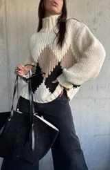 Sweater de punto grueso con cuello alto, diseño de rombos en tonos beige y negro sobre base color natural, de corte holgado y mangas largas con puños ajustados.