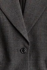 Blazer de mujer gris oscuro con estampado Príncipe de Gales (a cuadros). Presenta solapas de muesca, cierre frontal de dos botones, hombreras y bolsillos delanteros con solapa.