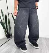 Pantalón jean baggy gris oscuro con diseño estampado de rayos en tono más claro, tiro medio y corte oversize.