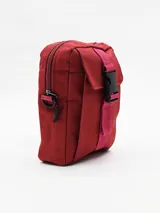 Morral color bordó con cierre superior y bolsillo frontal con solapa, asegurado con una tira de tela rosa y hebilla plástica negra.