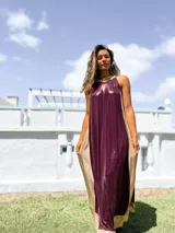 Vestido largo de fiesta con diseño bicolor, presentando un panel frontal en color bordó y paneles laterales en color dorado. Confeccionado en tela brillante con caída fluida, presenta escote halter y corte holgado.