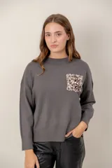 Sweater de punto color gris, con cuello redondo, mangas largas y un bolsillo frontal decorado con lentejuelas brillantes.