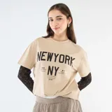 Camiseta de manga corta color beige con estampado gráfico frontal en negro, que incluye una segunda capa de mangas largas de encaje negro debajo.